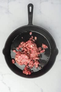 Raw ground beef and water added to a skillet, ready to break down into the fine-textured base for Coney Sauce Recipe.