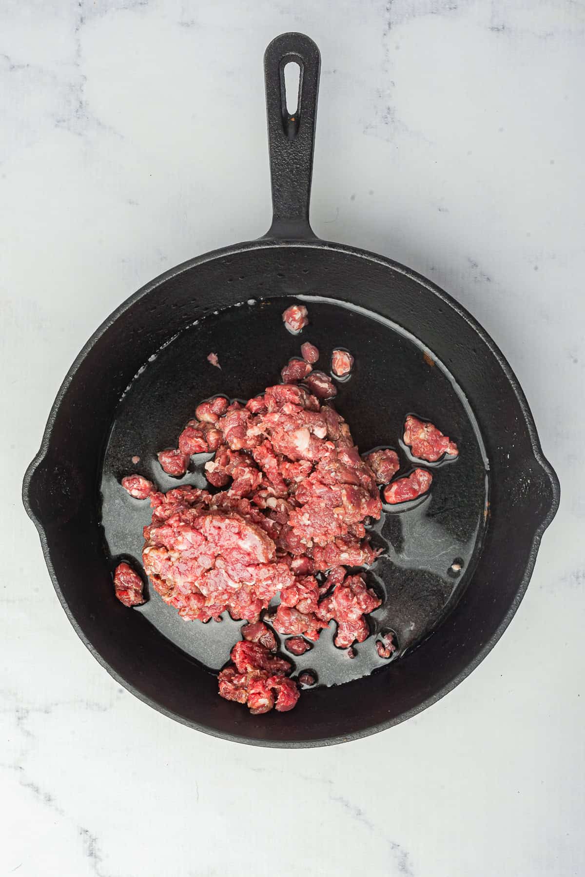 Raw ground beef and water added to a skillet, ready to break down into the fine-textured base for Hot Dog Sauce.