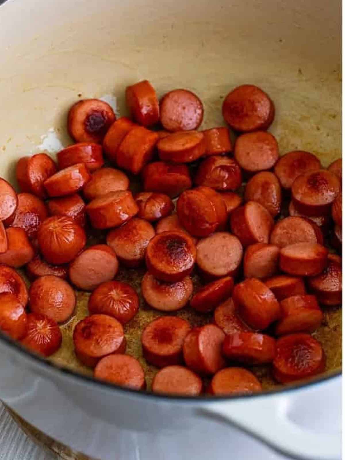 Searing sliced hot dogs in olive oil in a Dutch oven.