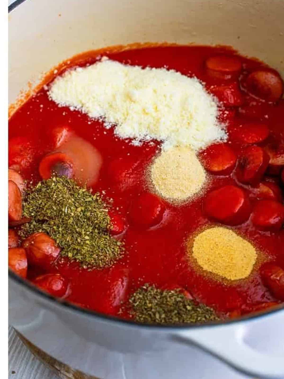 Adding tomato sauce, parmesan, and seasonings to the seared hot dogs.