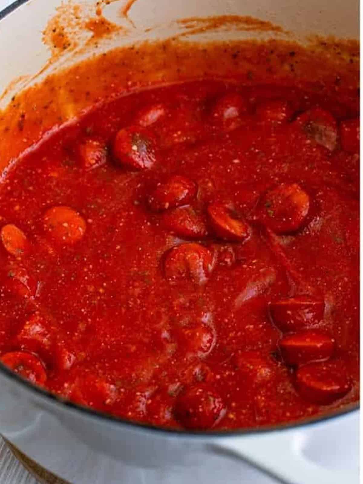 Simmering the hot dog spaghetti sauce until thickened.