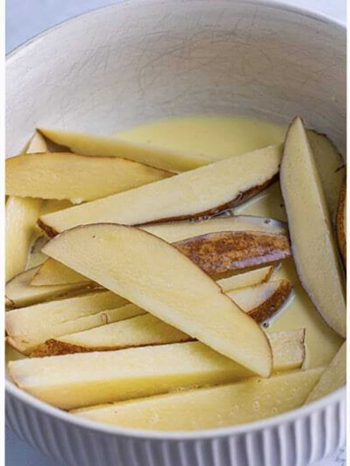 Cut russet potato wedges coated in the milk and egg wash for KFC potato wedges.