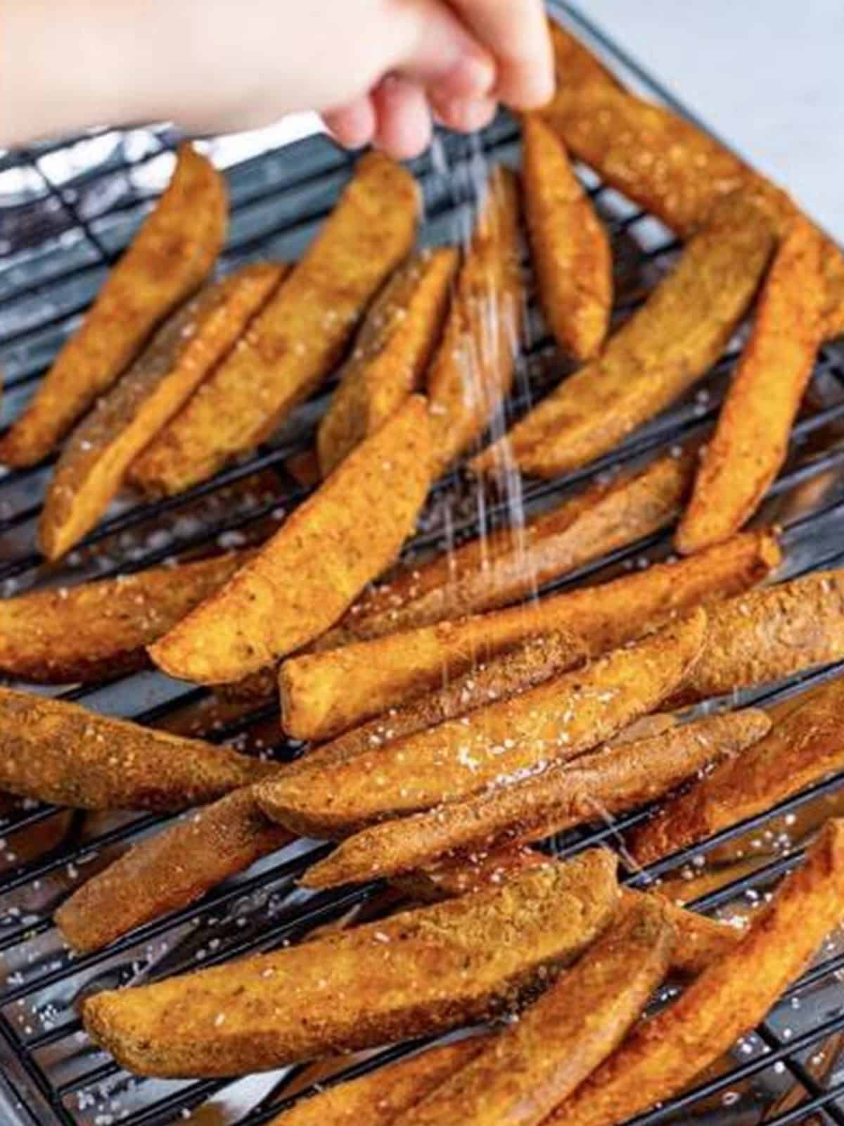 Crispy golden KFC potato wedges draining on a rack after the second fry.