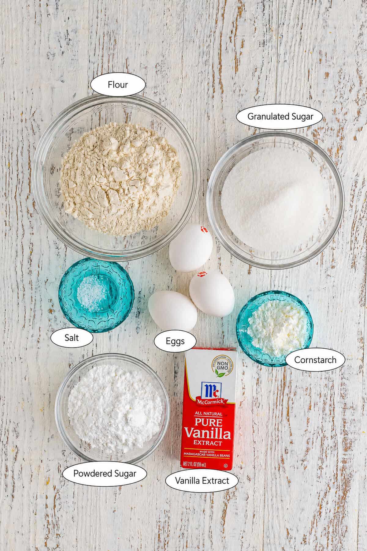 Homemade Lady Finger Cookies Recipe ingredients laid out on a marble counter including all-purpose flour, cornstarch, large eggs, granulated sugar, kosher salt, vanilla extract, and powdered sugar.