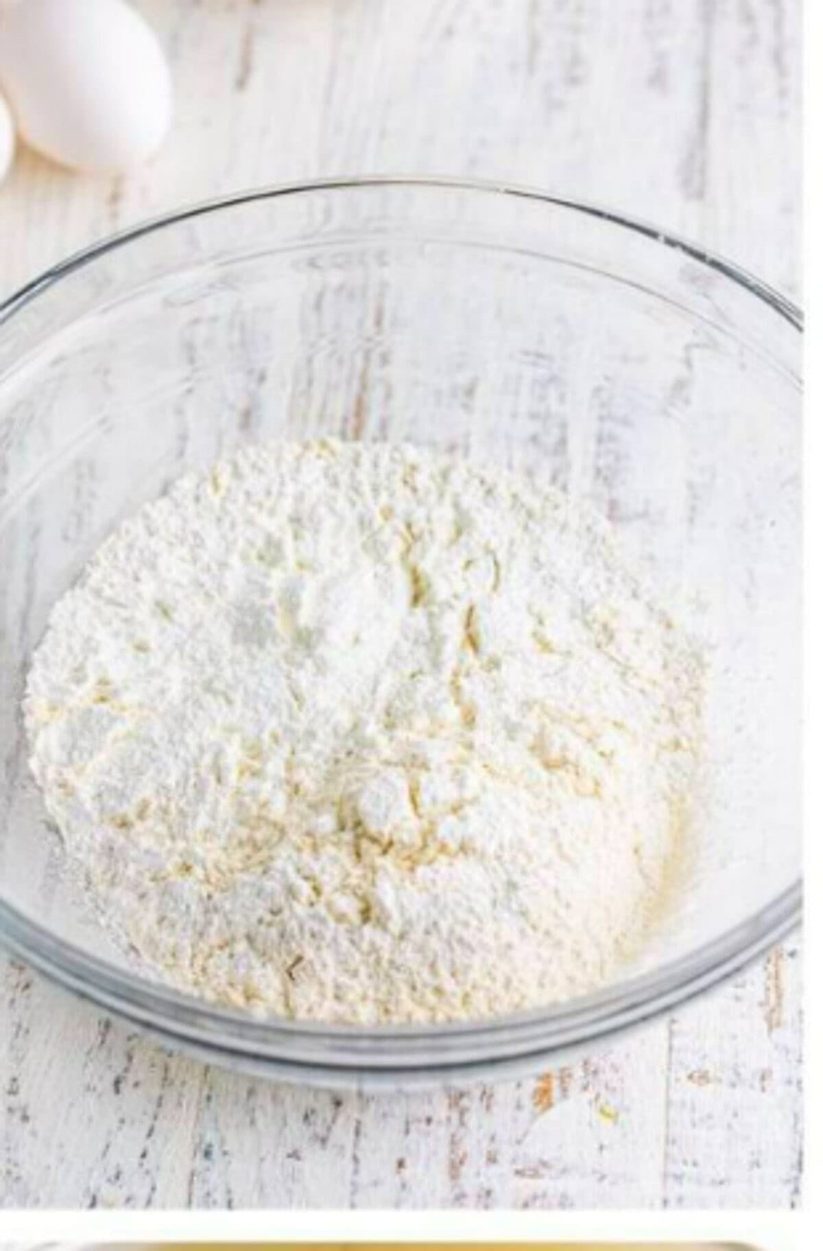Sheet trays lined with parchment paper next to a bowl of whisked sifted flour and cornstarch for the Homemade Lady Finger Cookies Recipe preheat and dry whisk step.