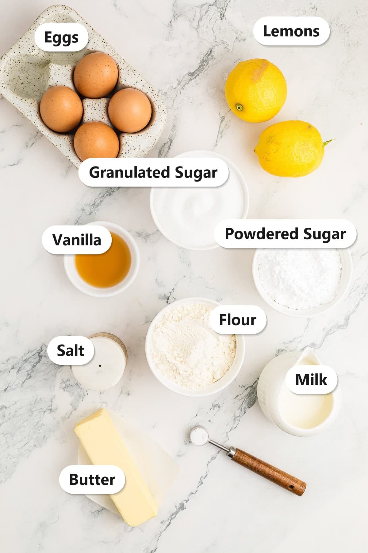 Labeled ingredients for lemon cake including eggs, lemons, sugar, powdered sugar, flour, milk, butter, vanilla, and salt.