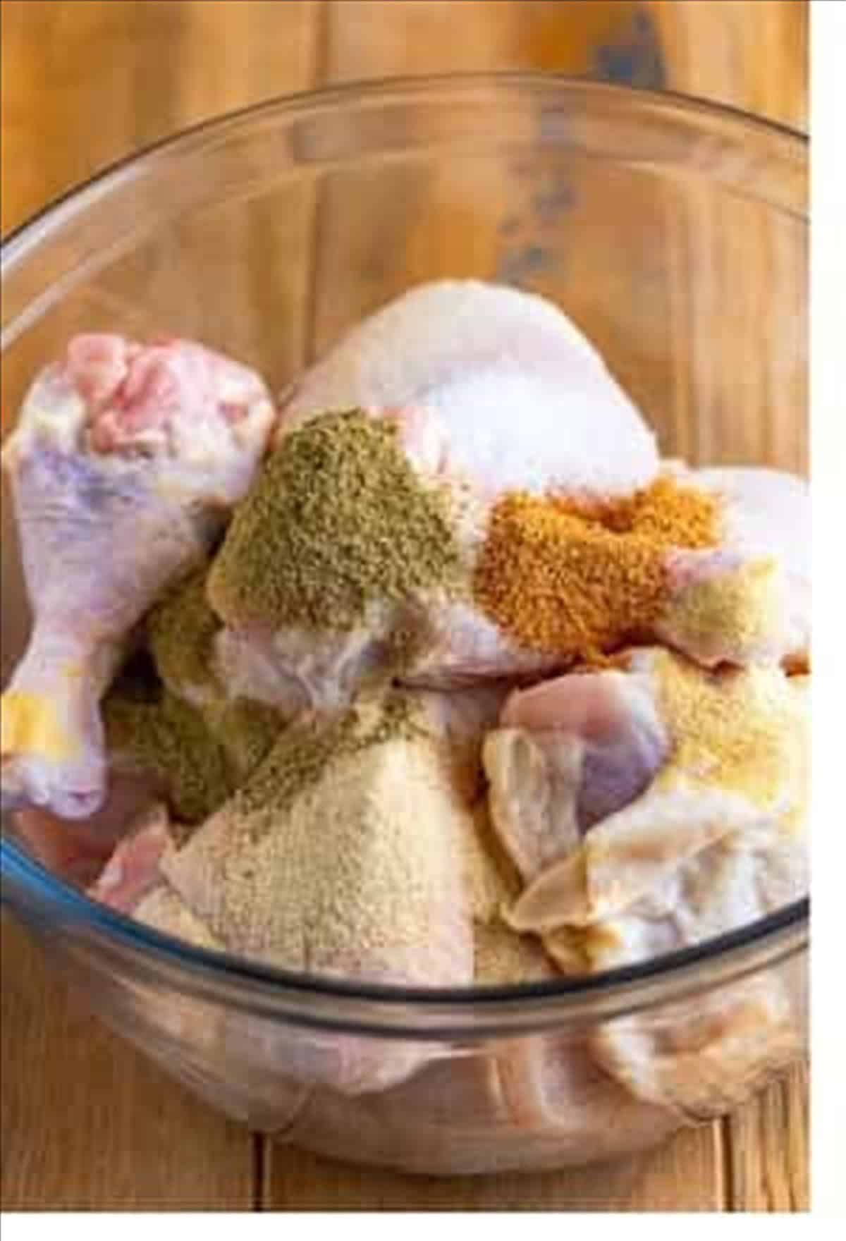 Chicken pieces tossed with creole seasoning, garlic powder, onion powder, and poultry seasoning in a glass bowl.