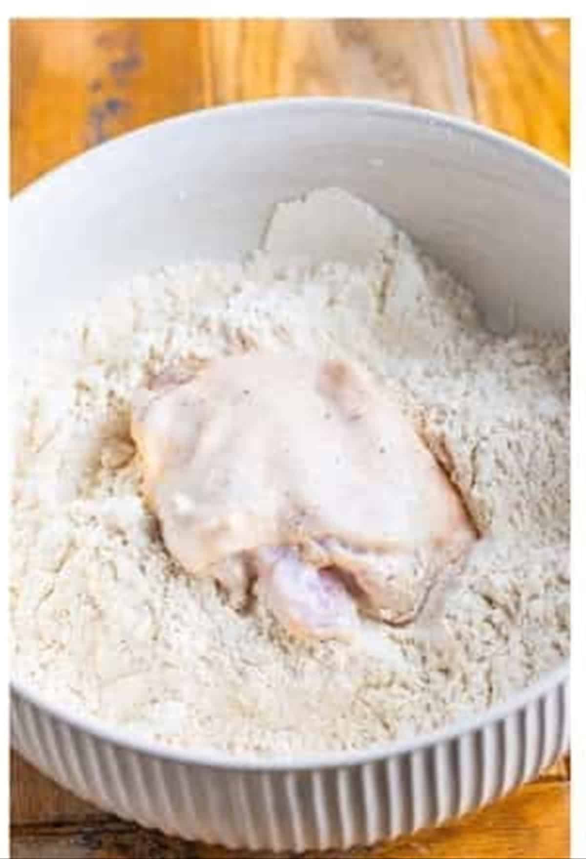 A marinated chicken piece pressed into the seasoned flour to coat for Louisiana fried chicken.