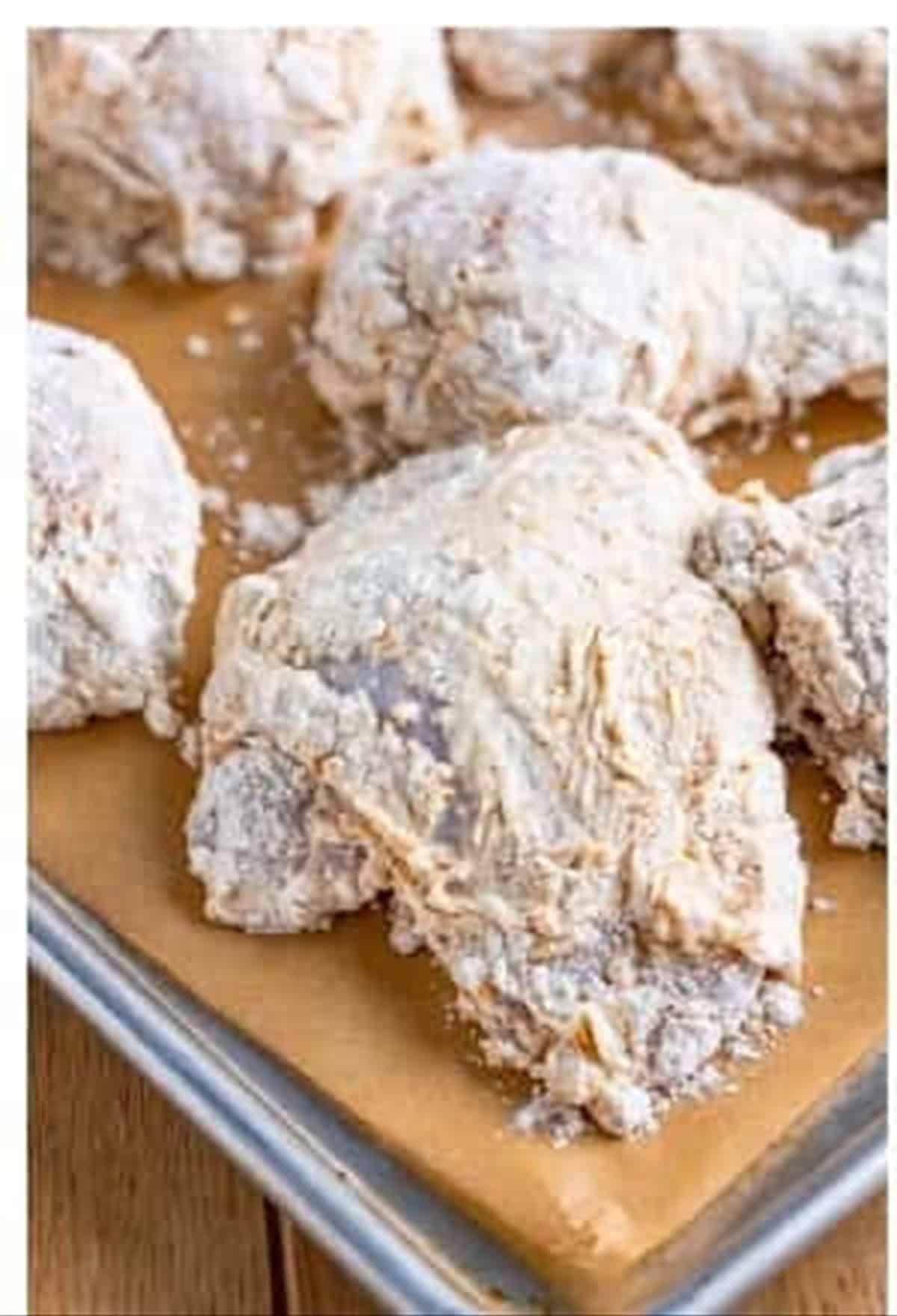 Breaded Louisiana fried chicken pieces resting on a parchment lined tray until pasty.