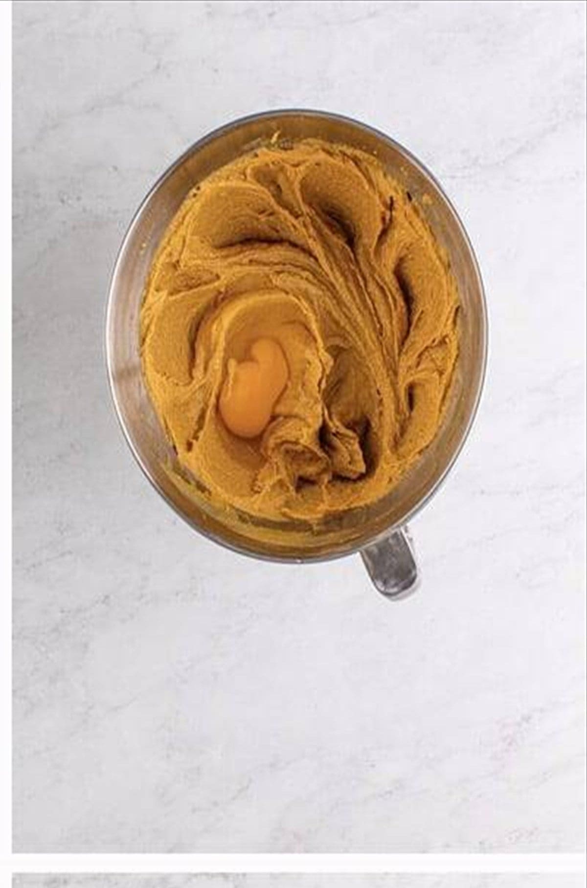 Egg added to peanut butter cookie dough in a stand mixer bowl.