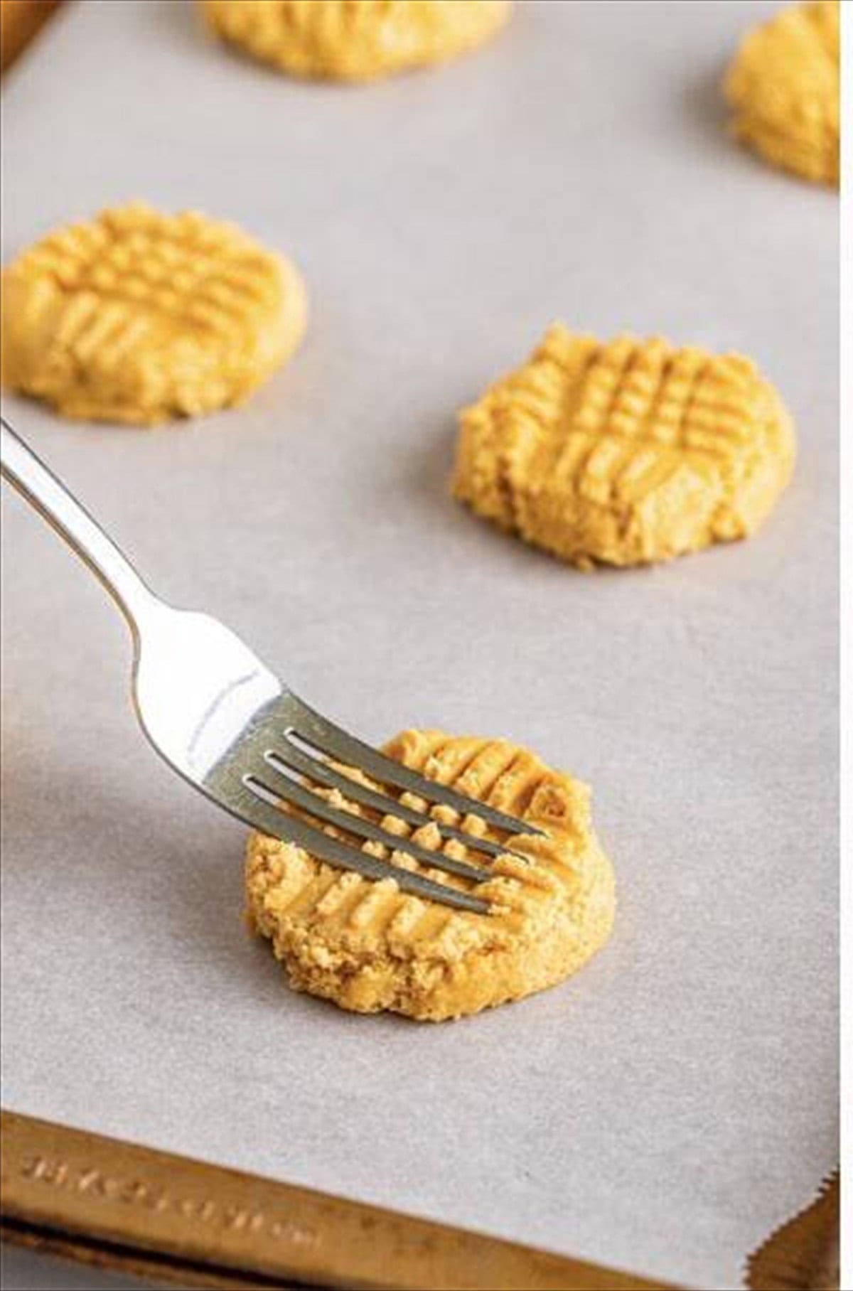 Fork creating crosshatch marks on peanut butter cookie dough ball on parchment.