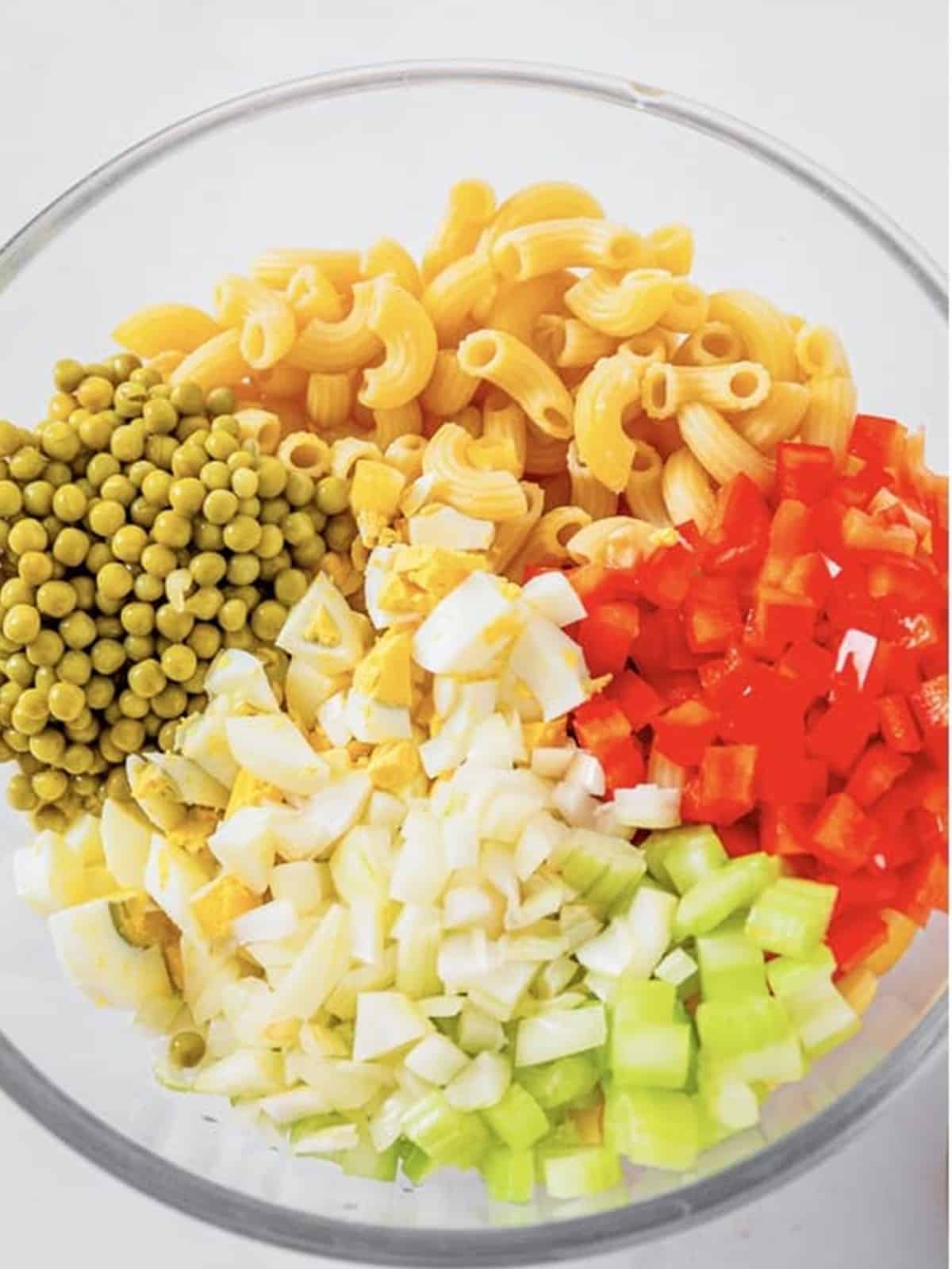 Macaroni peas bell pepper onion celery and egg combined in a bowl for macaroni salad.