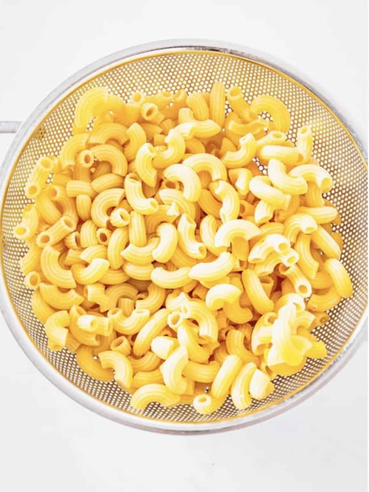 Cooked macaroni draining in a colander for creamy macaroni salad.