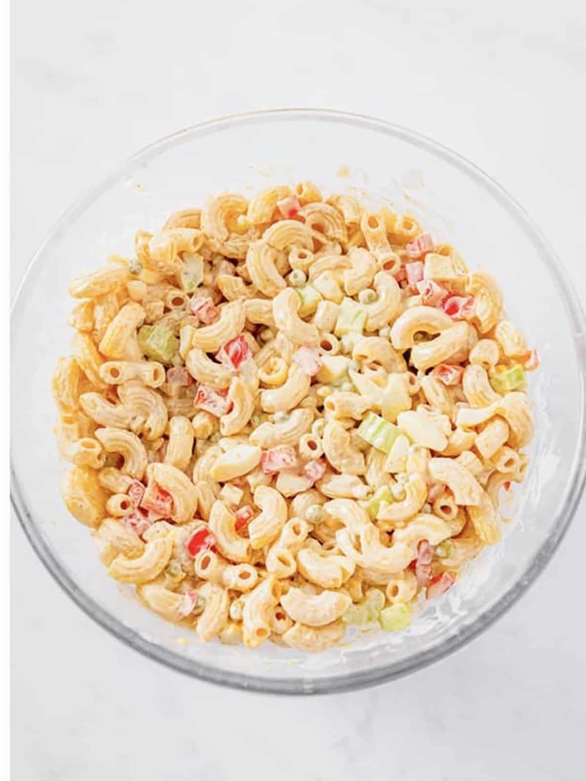 Creamy macaroni salad tossed with dressing in a glass bowl.