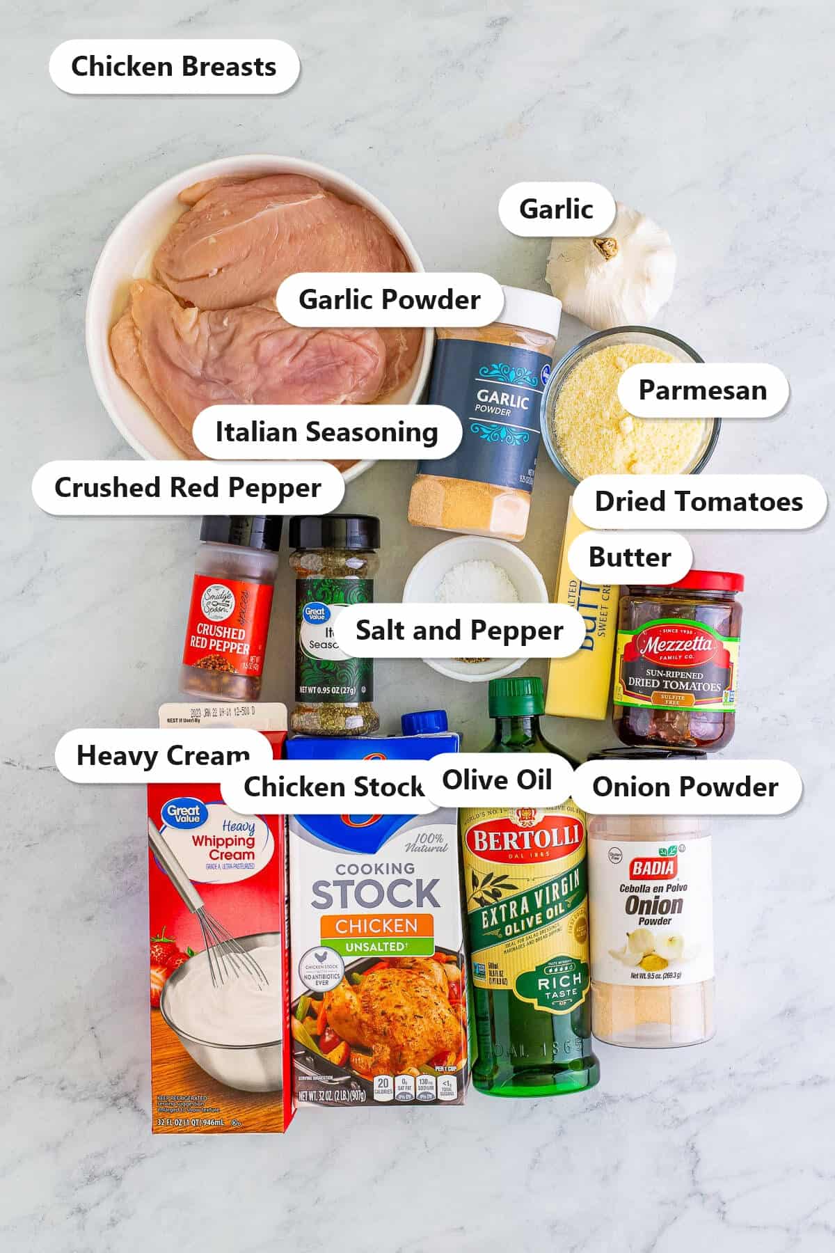 Labeled Marry Me Chicken ingredients including chicken breasts heavy cream sundried tomatoes Parmesan garlic chicken stock and Italian seasoning on a marble counter.