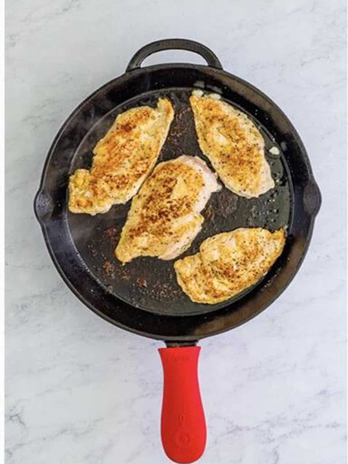 Searing seasoned chicken in a cast iron skillet for Marry Me Chicken.