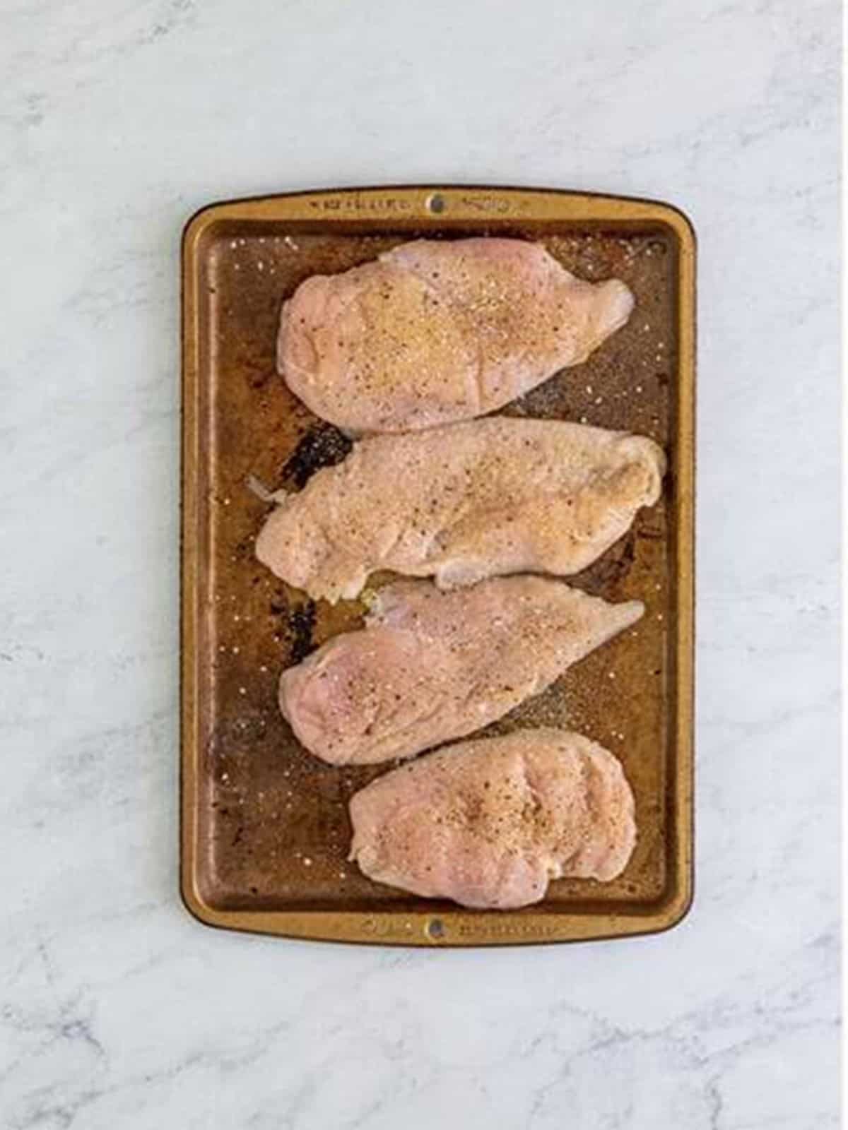 Seasoned chicken breasts on a baking sheet for Marry Me Chicken.