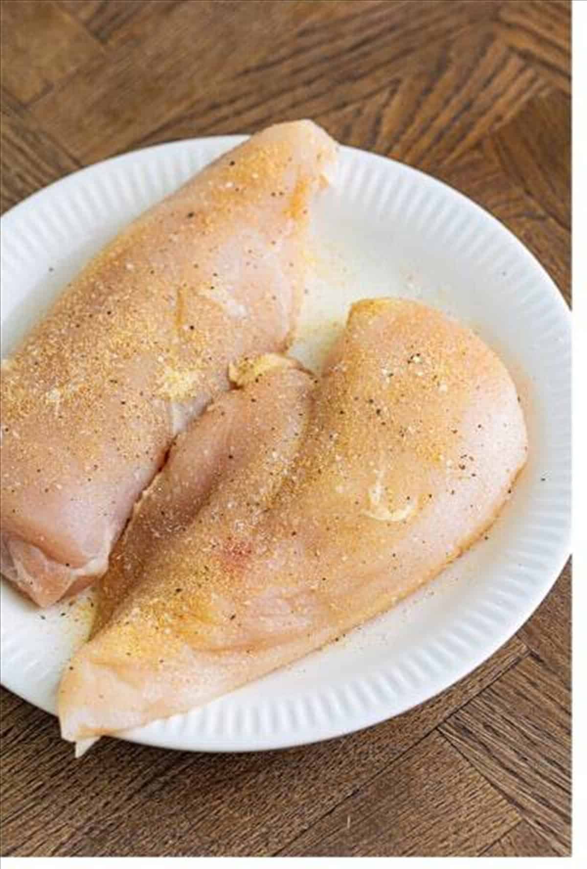 Seasoned chicken breasts on a plate ready to grill for Monterey chicken.