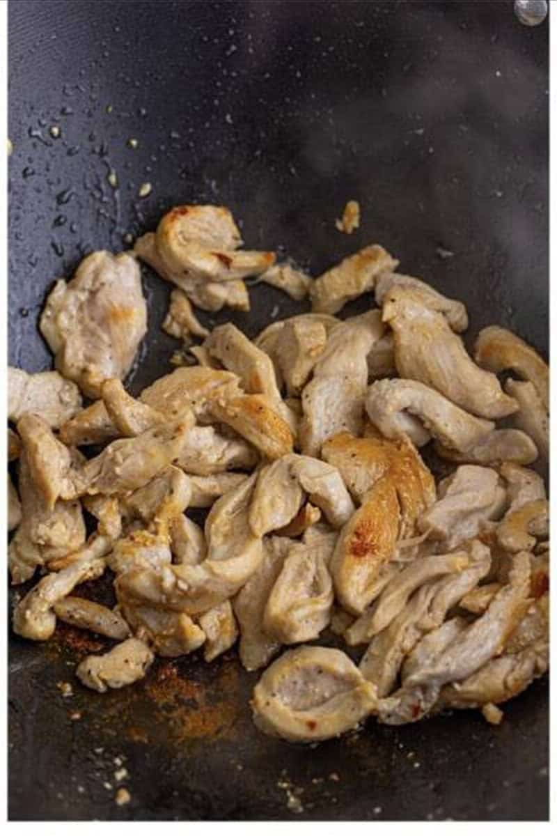 Seasoned chicken pieces browning in a hot wok for pancit recipe.