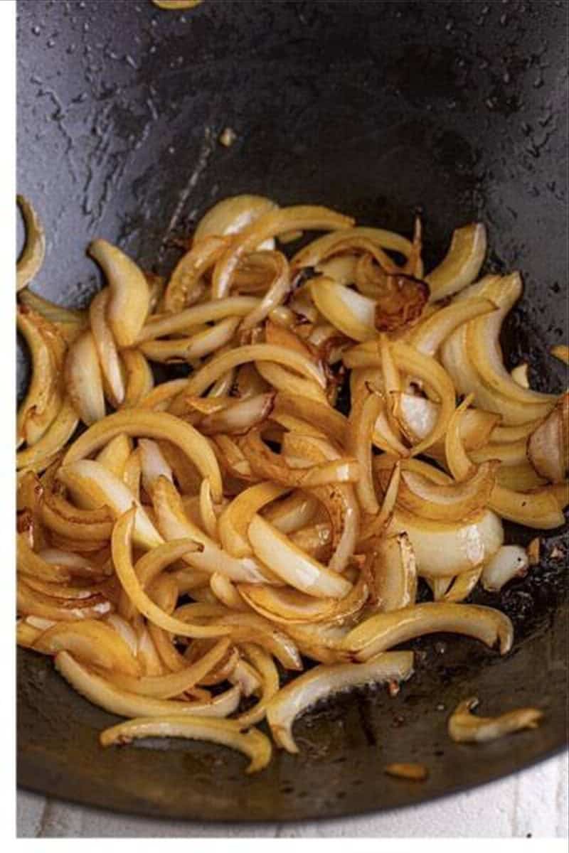 Sliced yellow onions sauteing in a wok until translucent for pancit recipe.