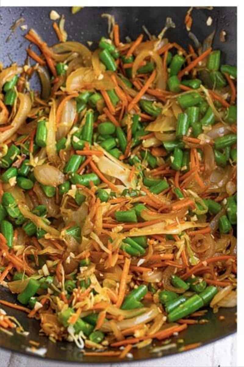 Green beans, shredded cabbage, and matchstick carrots cooking with onions in a wok for pancit recipe.