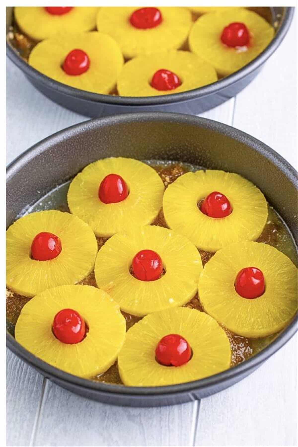 Pineapple slices arranged with maraschino cherries in the centers over the brown sugar butter layer for the upside down cake topping.