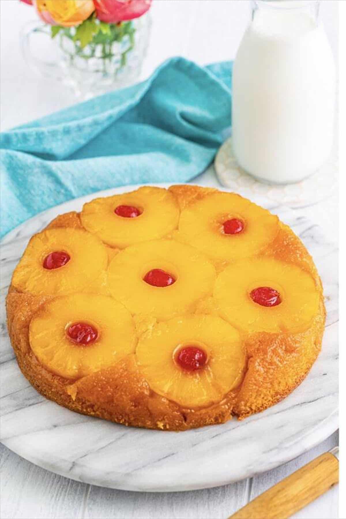 First Pineapple Upside Down Cake layer inverted onto a plate with pineapple slices and cherries showing on top for cake assembly.