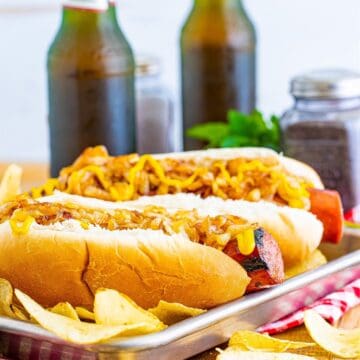 A pair of Polish Sausage Sandwich Recipe sandwiches with grilled sausage, caramelized onions, and yellow mustard on toasted hoagie rolls.