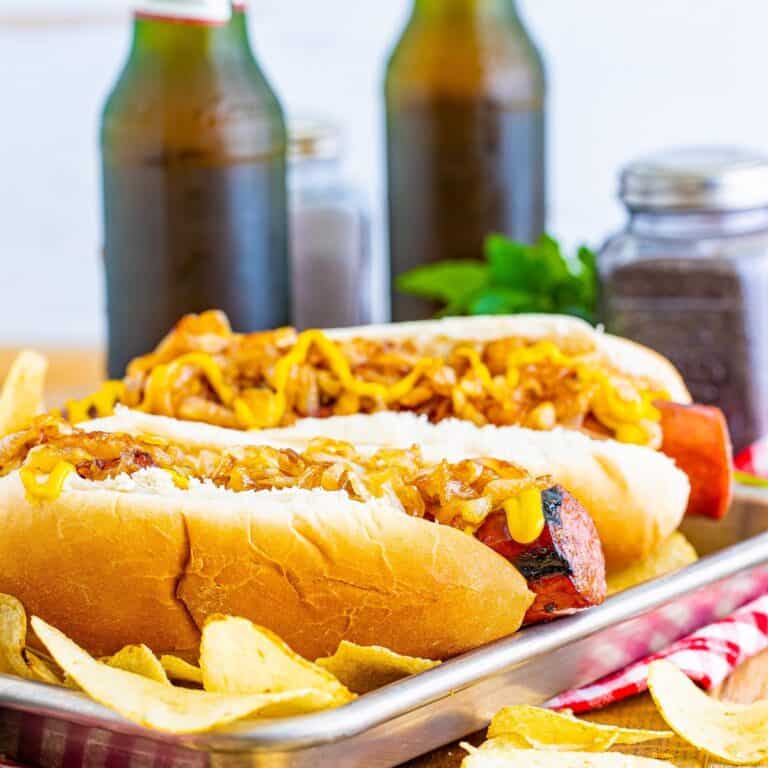 A pair of Polish Sausage Sandwich Recipe sandwiches with grilled sausage, caramelized onions, and yellow mustard on toasted hoagie rolls.