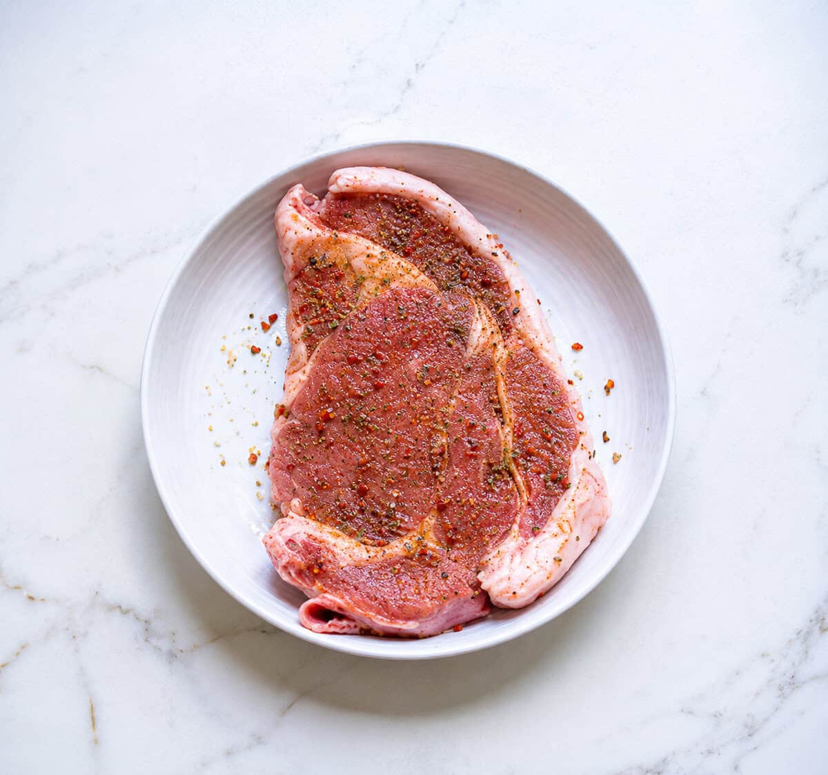 Bone-in ribeye steak seasoned with pepper, brown sugar, Montreal seasoning, and salt for the Ribeye Marinade.
