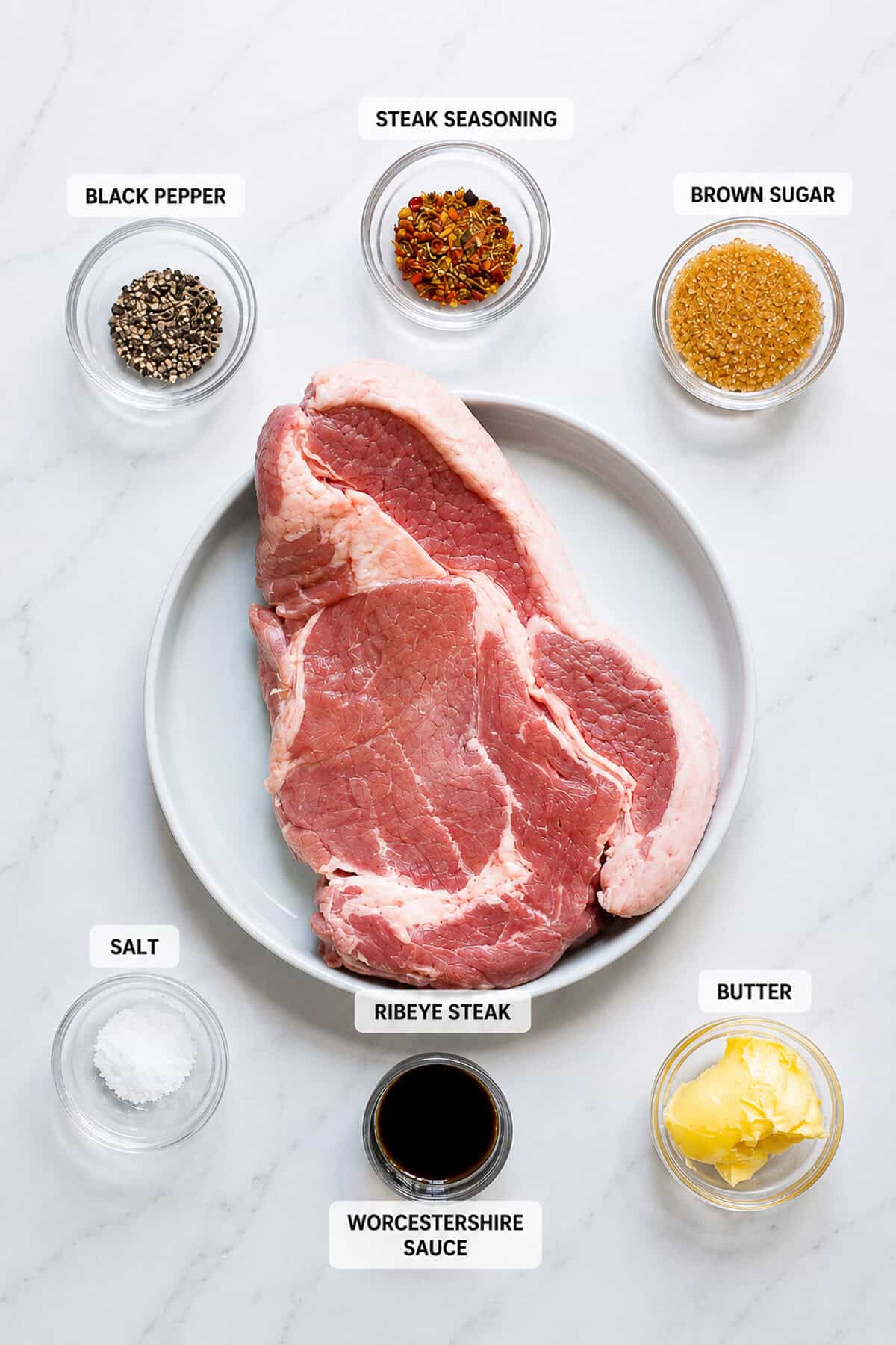 Labeled ingredients for Ribeye Marinade including bone-in ribeye steak, brown sugar, Worcestershire sauce, Montreal seasoning, black pepper, kosher salt, and butter.