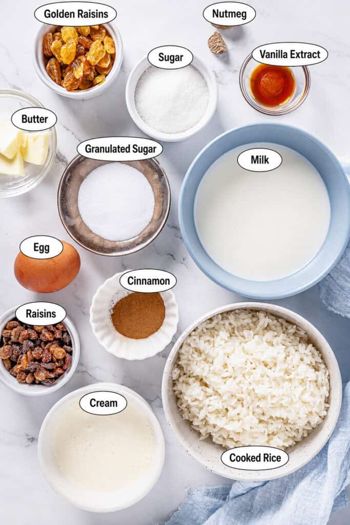 Labeled ingredients for Rice Pudding Recipe including cooked white rice, milk, heavy cream, eggs, sugar, raisins, butter, vanilla, cinnamon, and nutmeg.