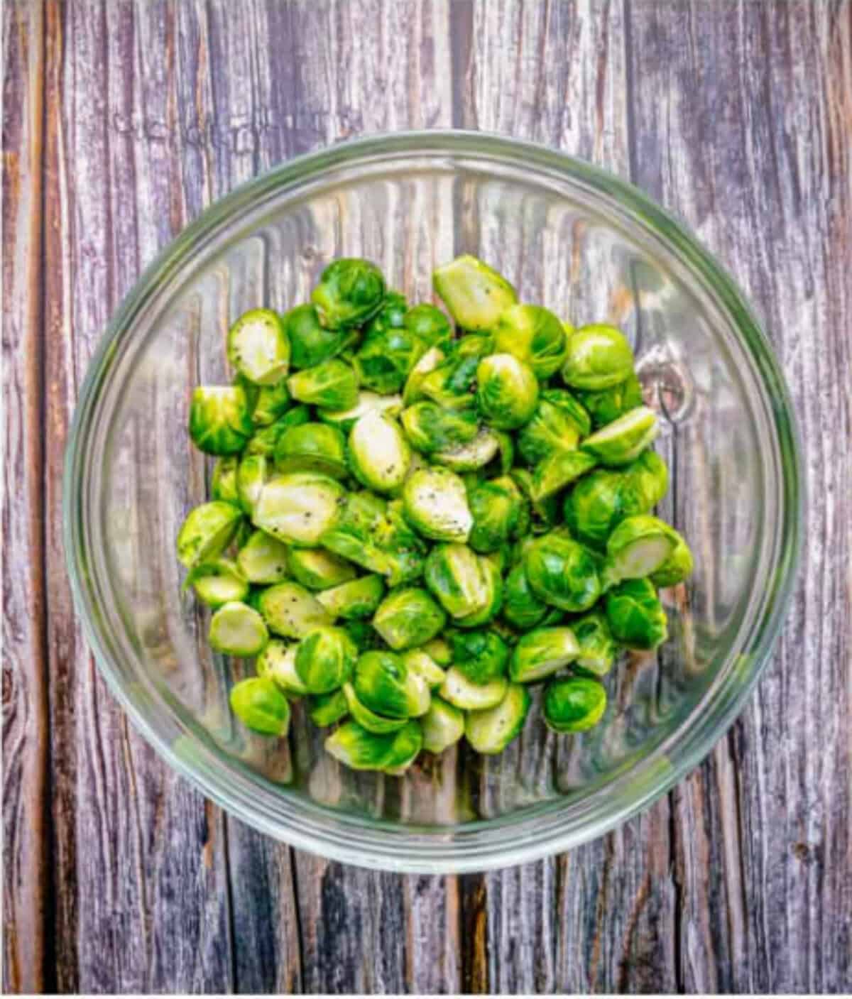 Fresh brussel sprouts cut in half lengthwise and tossed in a large bowl with olive oil, kosher salt, and black pepper for an Easy Oven Roasted Brussel Sprouts Recipe.