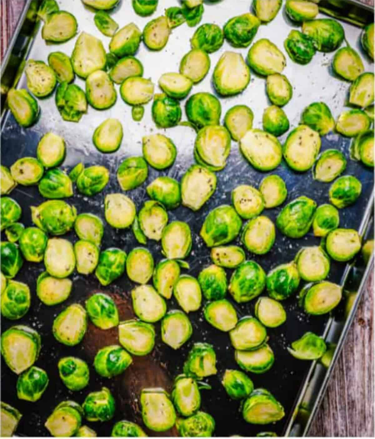 Halved brussel sprouts spread in a single layer across a large sheet tray, cut side down, ready to roast at 375 degrees for the Easy Oven Roasted Brussel Sprouts Recipe.