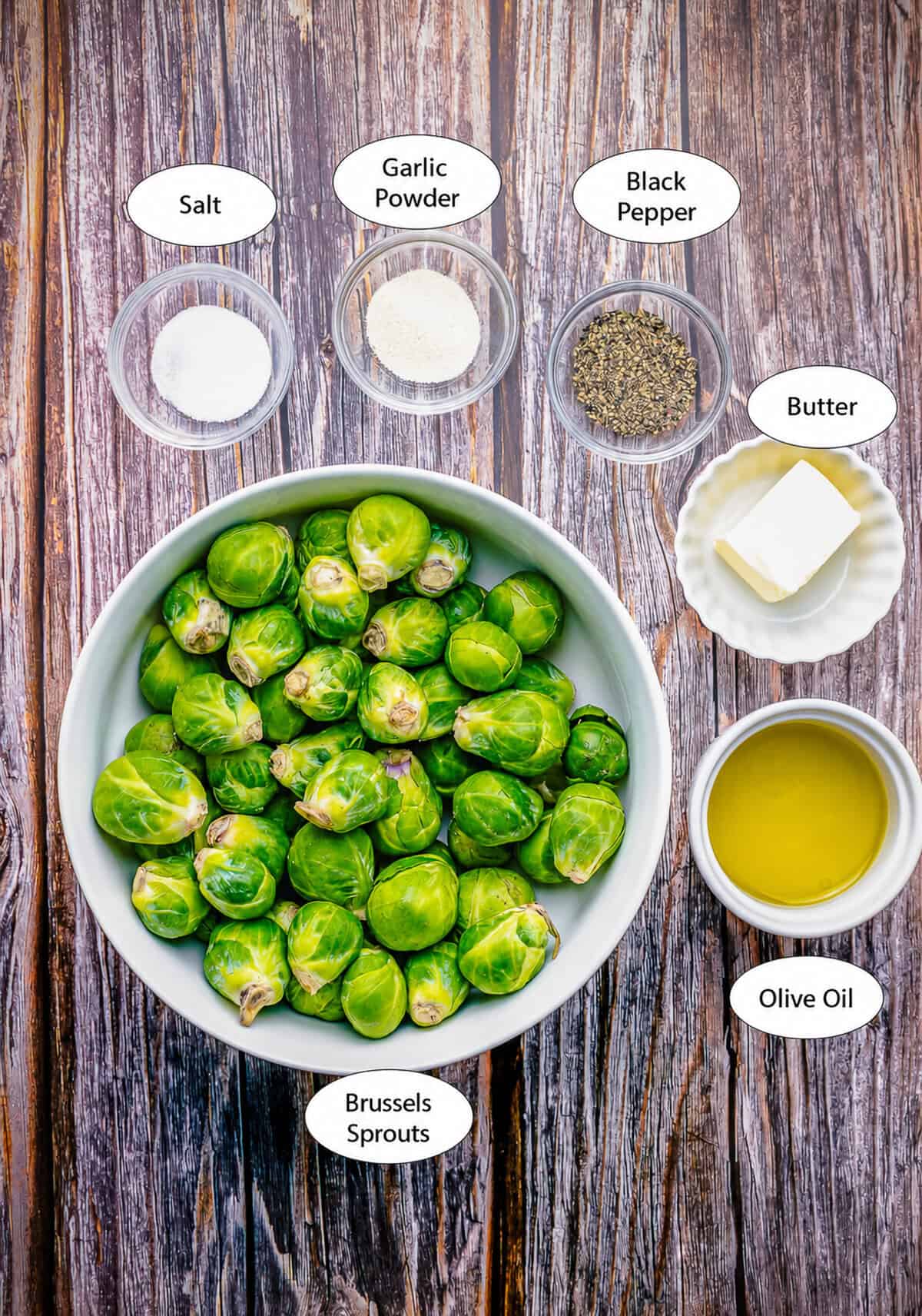 Easy Oven Roasted Brussel Sprouts Recipe ingredients laid out on a marble counter including fresh brussel sprouts, olive oil, kosher salt, black pepper, butter, and garlic powder.