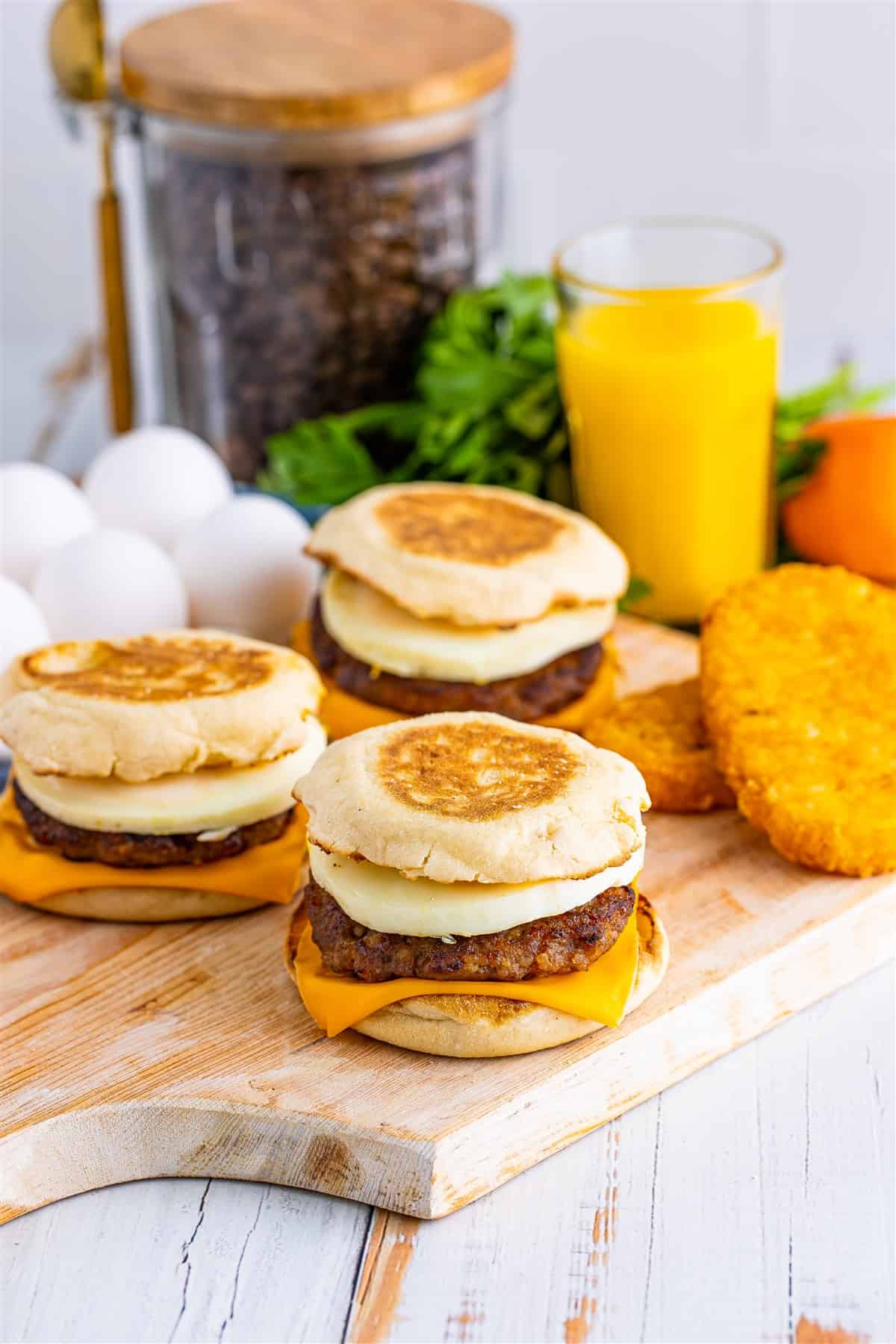 Stacked Sausage Egg McMuffin Recipe sandwiches plated with hash browns and orange juice glasses on a breakfast table.