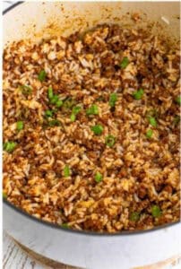 Adding cooked rice to the finished Sausage Rice Recipe sauce and stirring to combine.