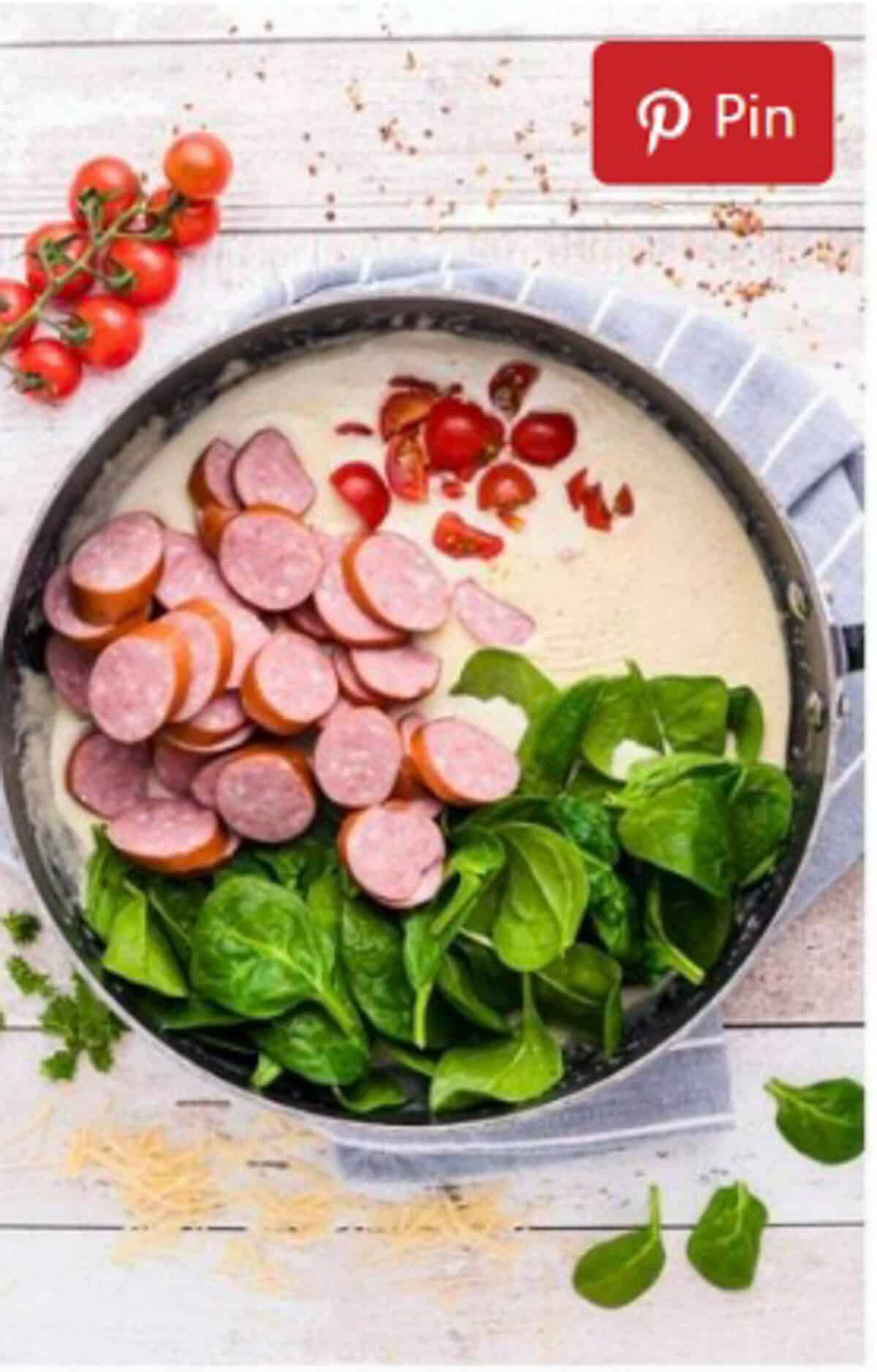 Sliced kielbasa, grape tomatoes, fresh spinach, and seasonings added to the creamy parmesan sauce in the pot.