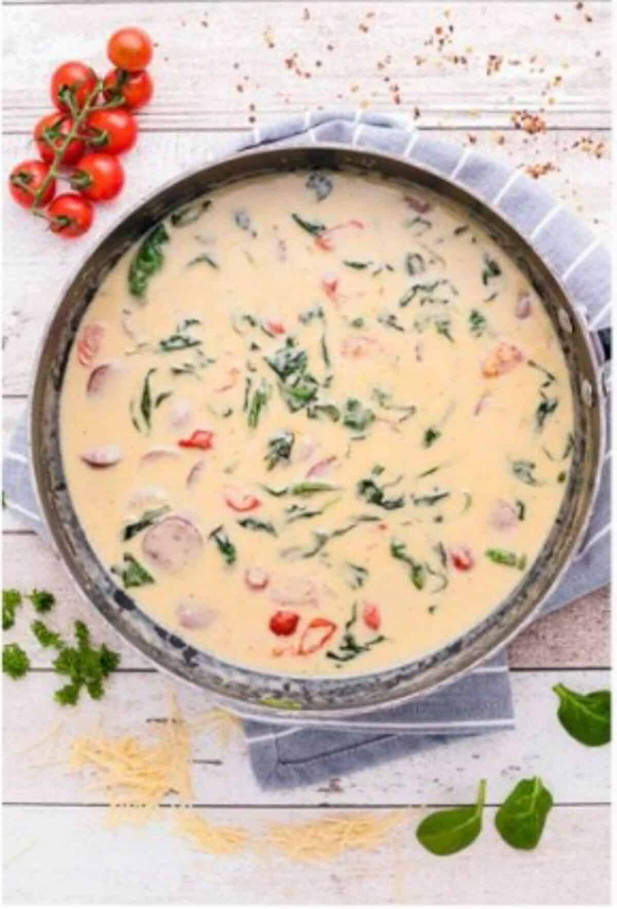 Spinach wilted into the creamy sauce with sliced kielbasa, tomatoes, and drained farfalle being folded into the pot.