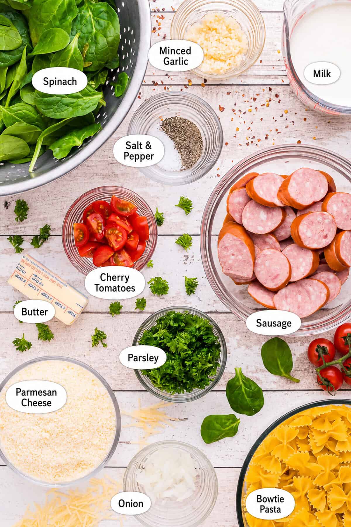 Labeled ingredients for Creamy Kielbasa Pasta including farfalle, kielbasa, heavy cream, parmesan, spinach, grape tomatoes, garlic, onion, butter, lemon, parsley, and seasonings.
