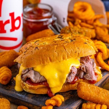 Copycat Arbys Beef and Cheddar Sandwich Recipe served on a fluffy onion bun with warm shaved roast beef piled high, a generous drizzle of homemade cheddar cheese sauce, and a swipe of tangy Arbys-style red sauce.