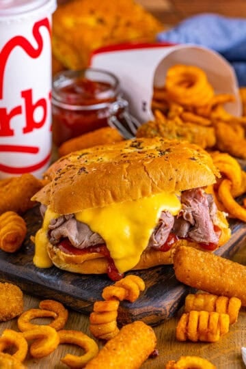 Copycat Arbys Beef and Cheddar Sandwich Recipe served on a fluffy onion bun with warm shaved roast beef piled high, a generous drizzle of homemade cheddar cheese sauce, and a swipe of tangy Arbys-style red sauce.