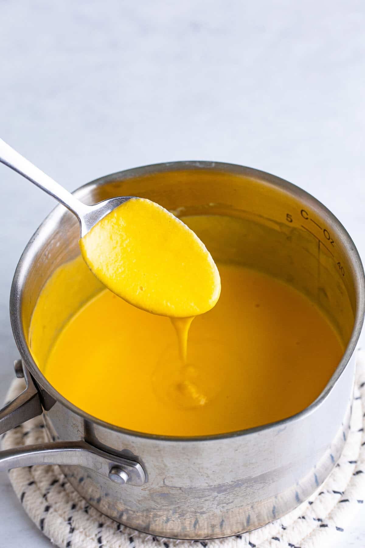 Homemade copycat Arbys cheddar cheese sauce coating a spoon in a saucepan after melting and thickening with milk.