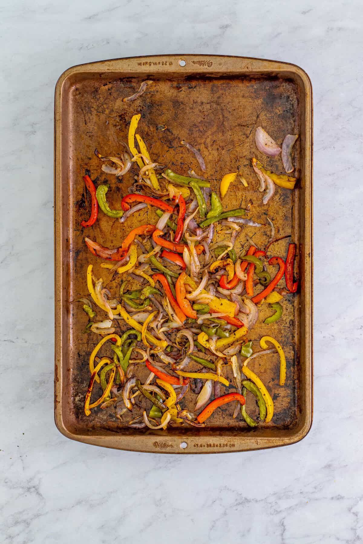 Sliced bell peppers and red onion tossed with olive oil and seasoning on a sheet pan for a Chipotle Bowl Recipe.