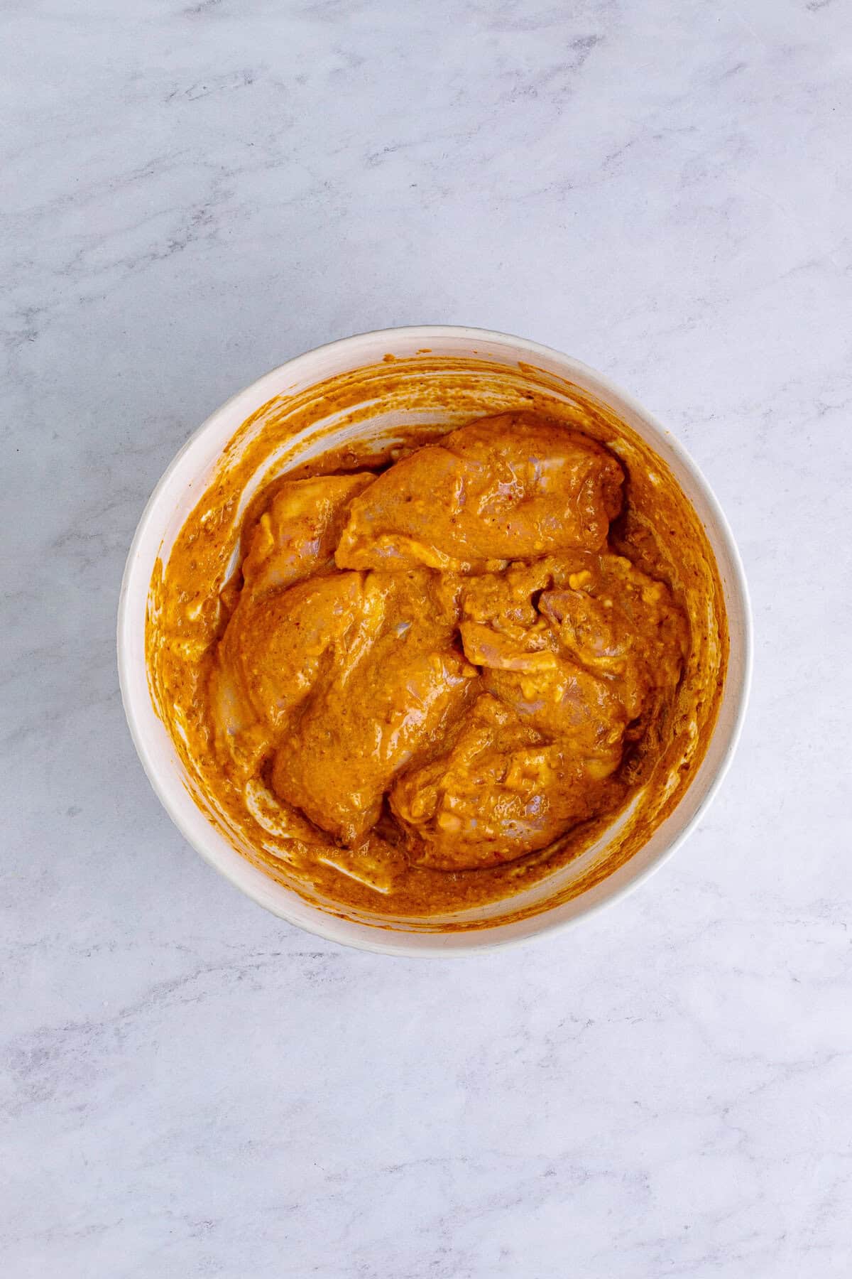 Chicken thighs trimmed in a bowl with the chipotle in adobo marinade whisked alongside for a Chipotle Bowl Recipe.