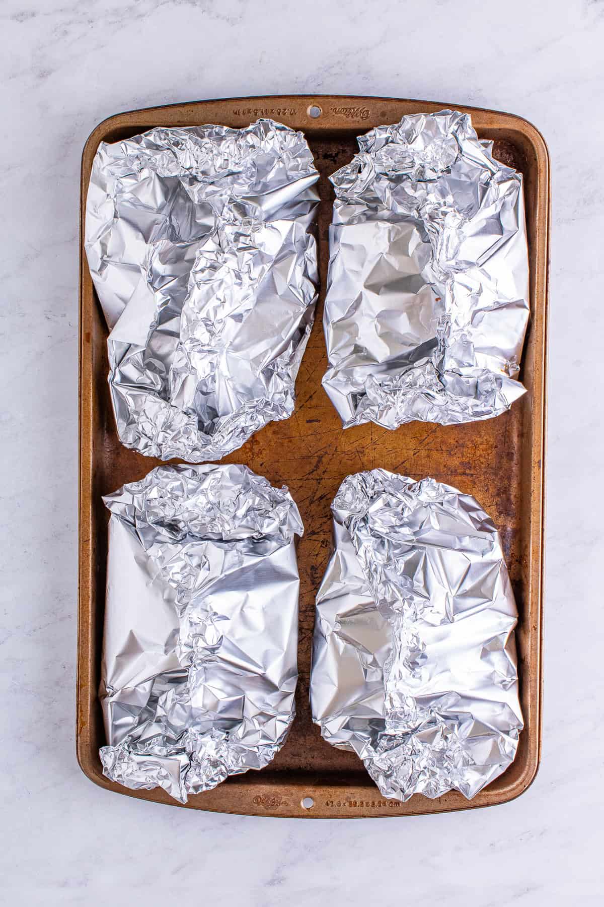 Sealed hamburger foil packets on a baking sheet ready to bake