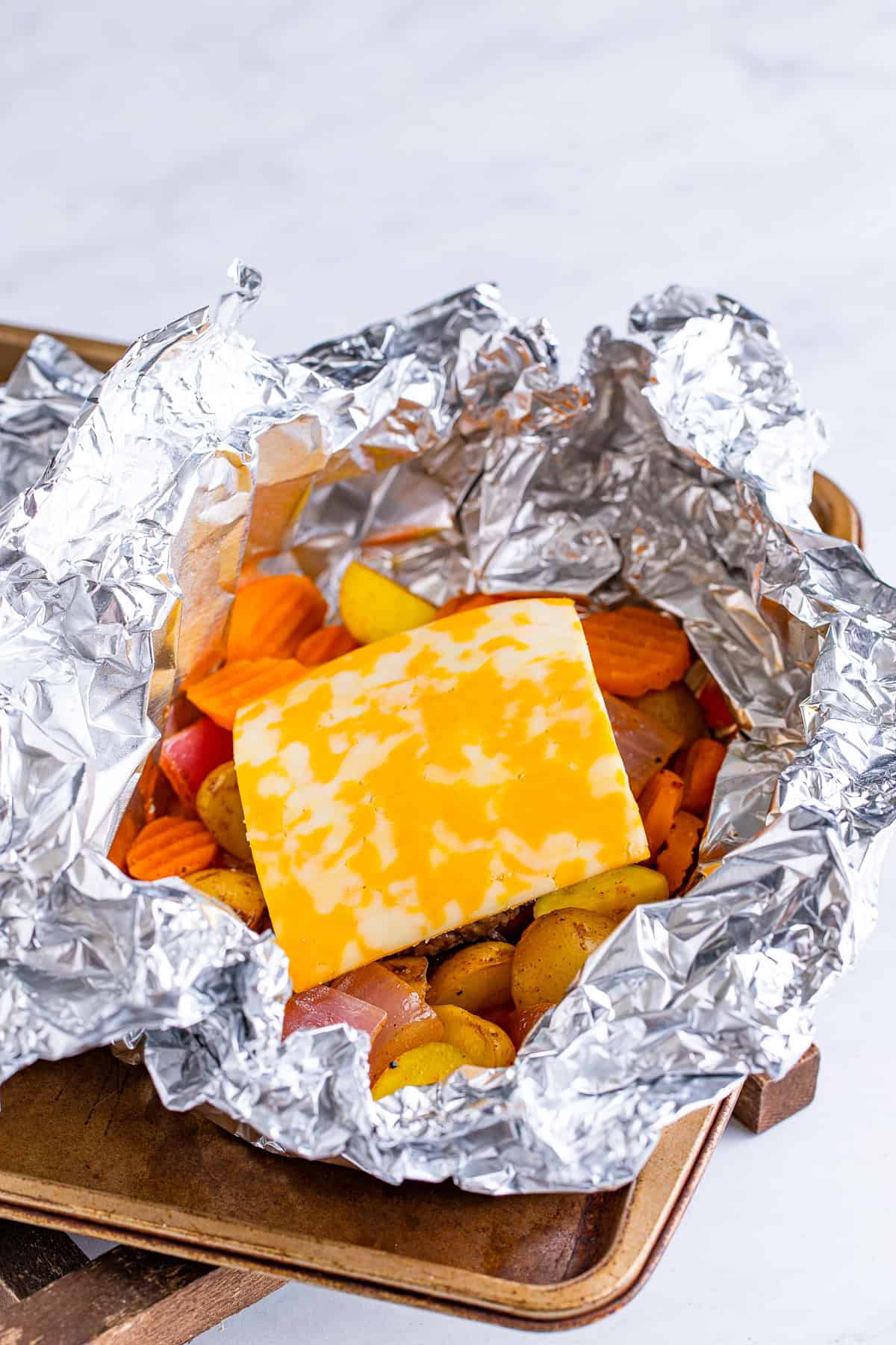 Opened hamburger foil packet topped with a slice of melting Colby Jack cheese