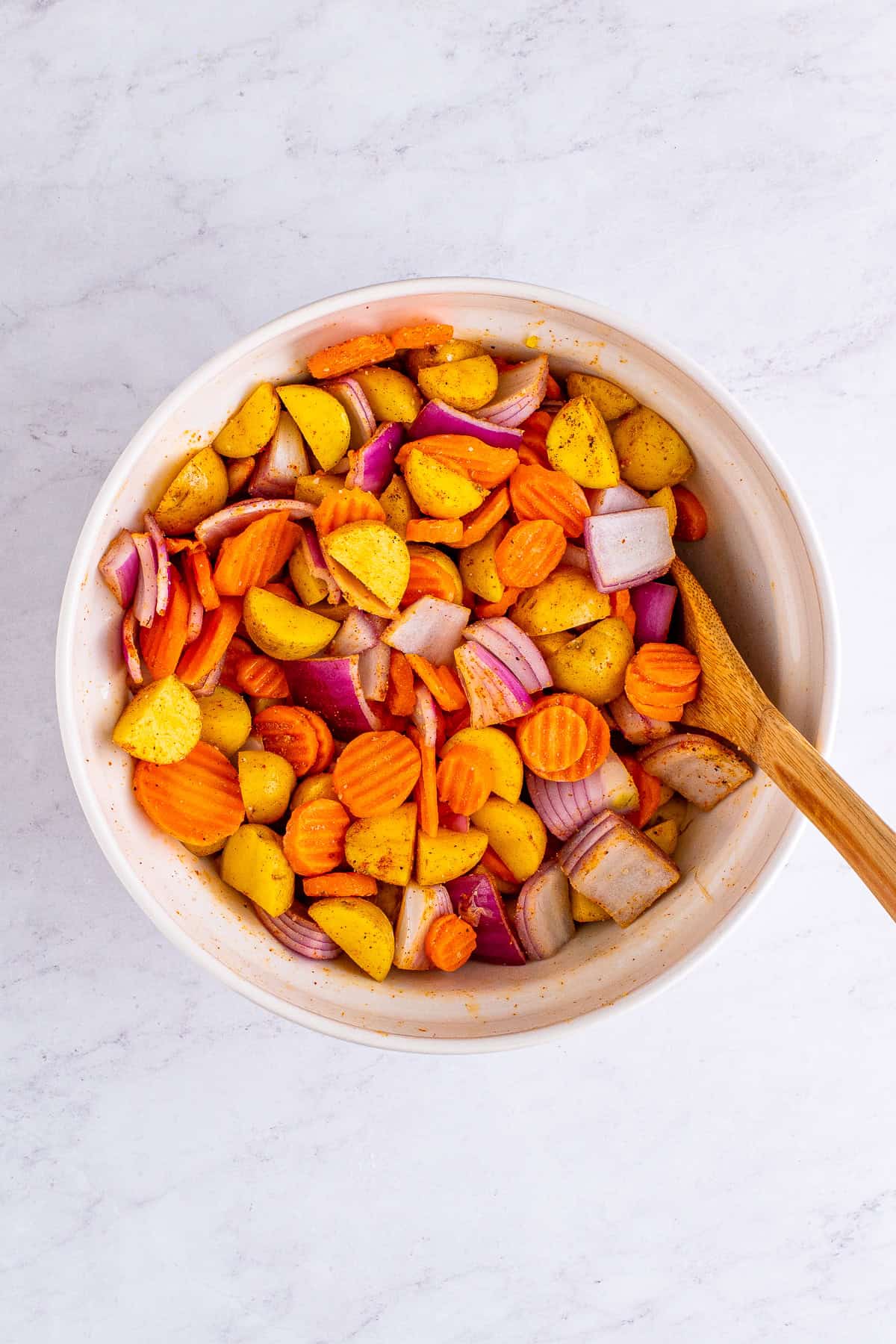 Diced potatoes, carrots, and red onion tossed with seasoning in a bowl