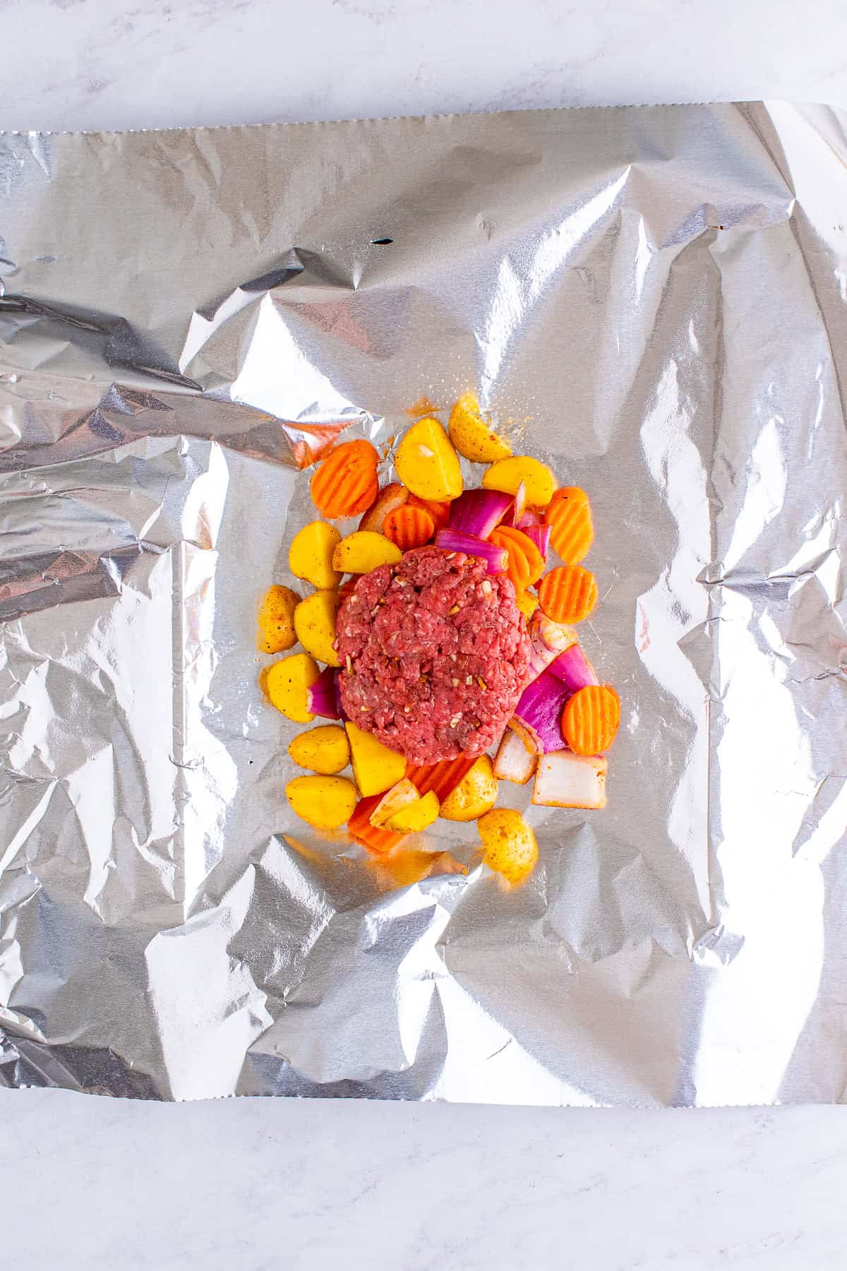 Ground beef patty placed on the vegetables on a foil sheet for a hamburger foil packet