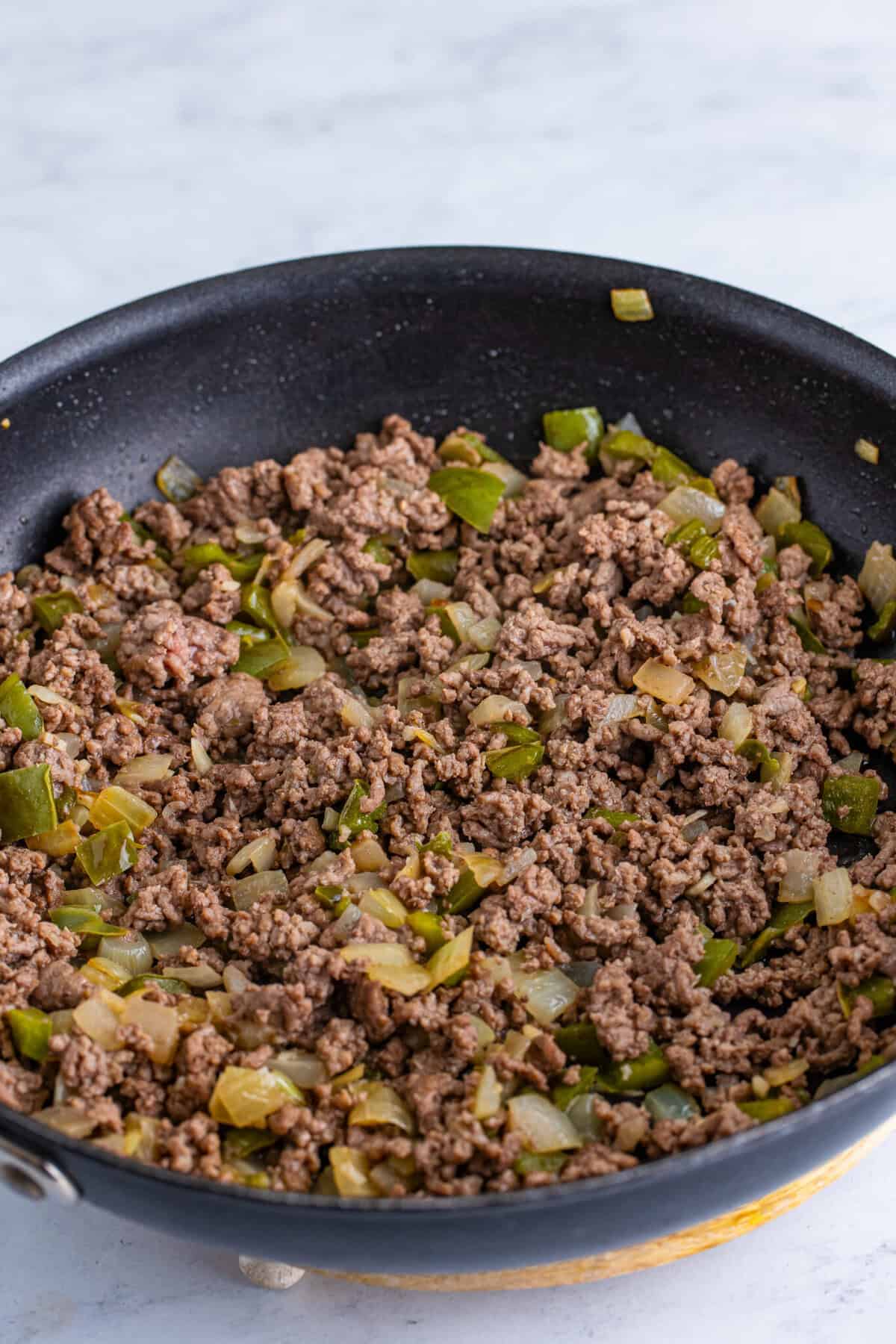 Fully browned and crumbled ground beef cooked with softened diced onion and green bell pepper in a dark nonstick skillet, no pink remaining.